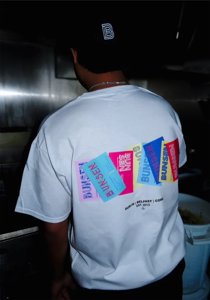Person wearing a Bunsen t-shirt and black cap with bright designs, highlighting locations: Dublin, Belfast, Cork.